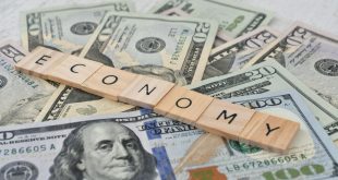The word ECONOMY spelled out in wooden letter tiles on a pile of cash money currency