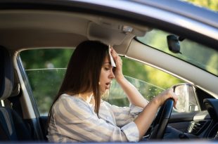 Woman driver being hot during heat wave in car, suffering from hot weather wipes sweat from forehead