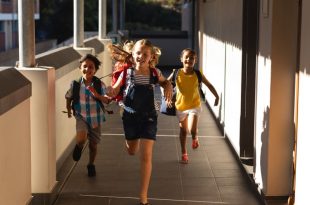 Front view of schoolkids with schoolbags running in hallway of elementary school