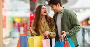 Joyful Couple On Shopping Laughing Holding Shopper Bags In Hypermarket