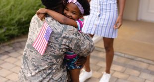 Army soldier embracing african american girl with usa flag at house entrance