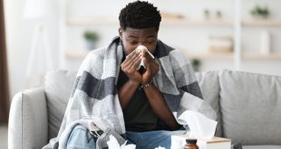 Sick black guy sitting at couch, sneezing