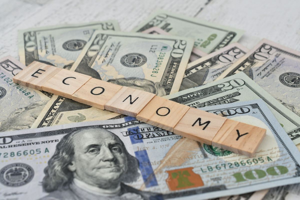 the word economy spelled out in wooden letter tiles on a pile of cash money currency