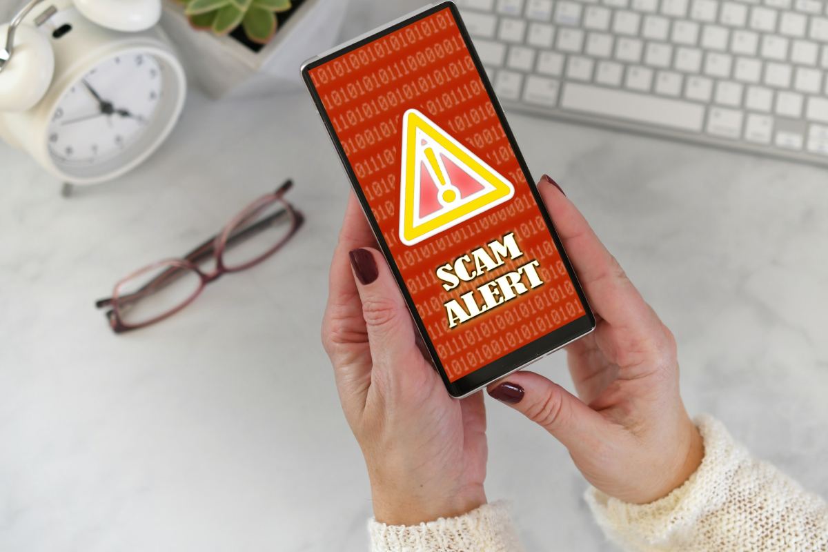 female holding a phone at desk with scam alert warning screen in red and yellow