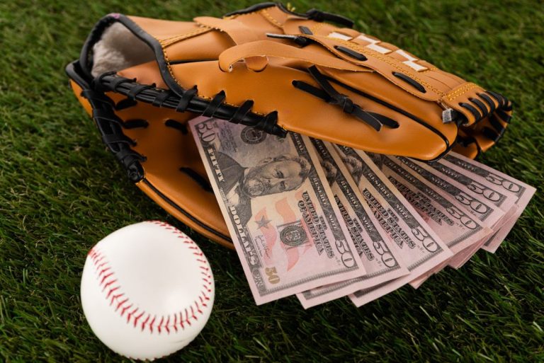 dollar banknotes in baseball glove near ball on green grass, sports betting concept