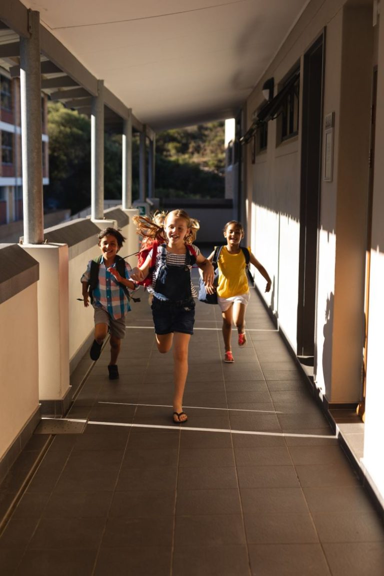 front view of schoolkids with schoolbags running in hallway of elementary school