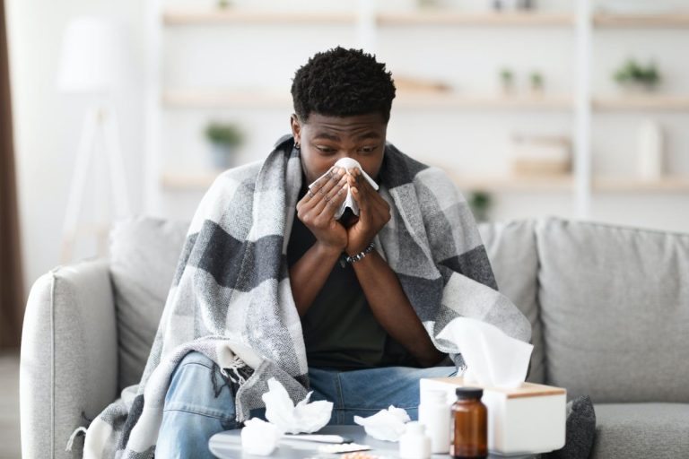 sick black guy sitting at couch, sneezing