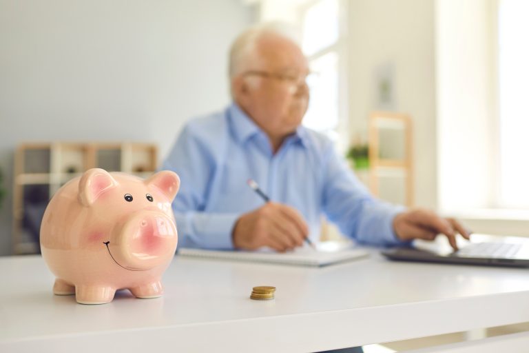 piggy,bank,in,soft,focus,on,desk,with,blurred,elderly