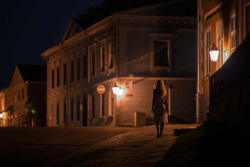 young,alone,woman,in,white,dress,slowly,walking,on,sidewalk